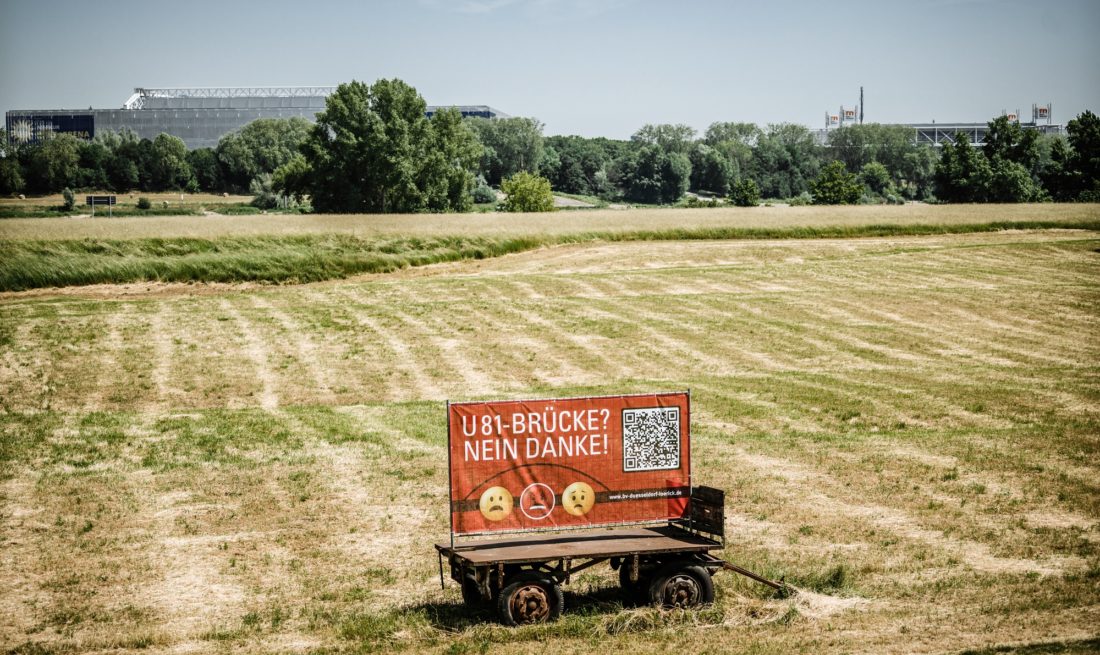 Etwa an der Stelle, auf dem Bürger*innen gegen eine U81-Brücke protestieren, würde das Bauwerk über den Rhein kommen. Im Hintergrund: Arena und Messe. Foto: Andreas Endermann